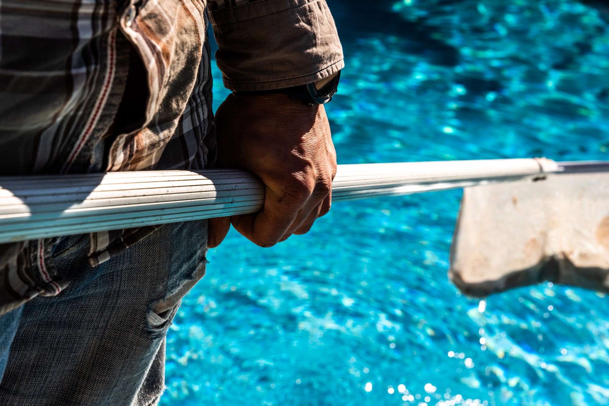 Maintenance man using a pool net leaf skimmer rake in summer to leave ready for bathing his pool.
